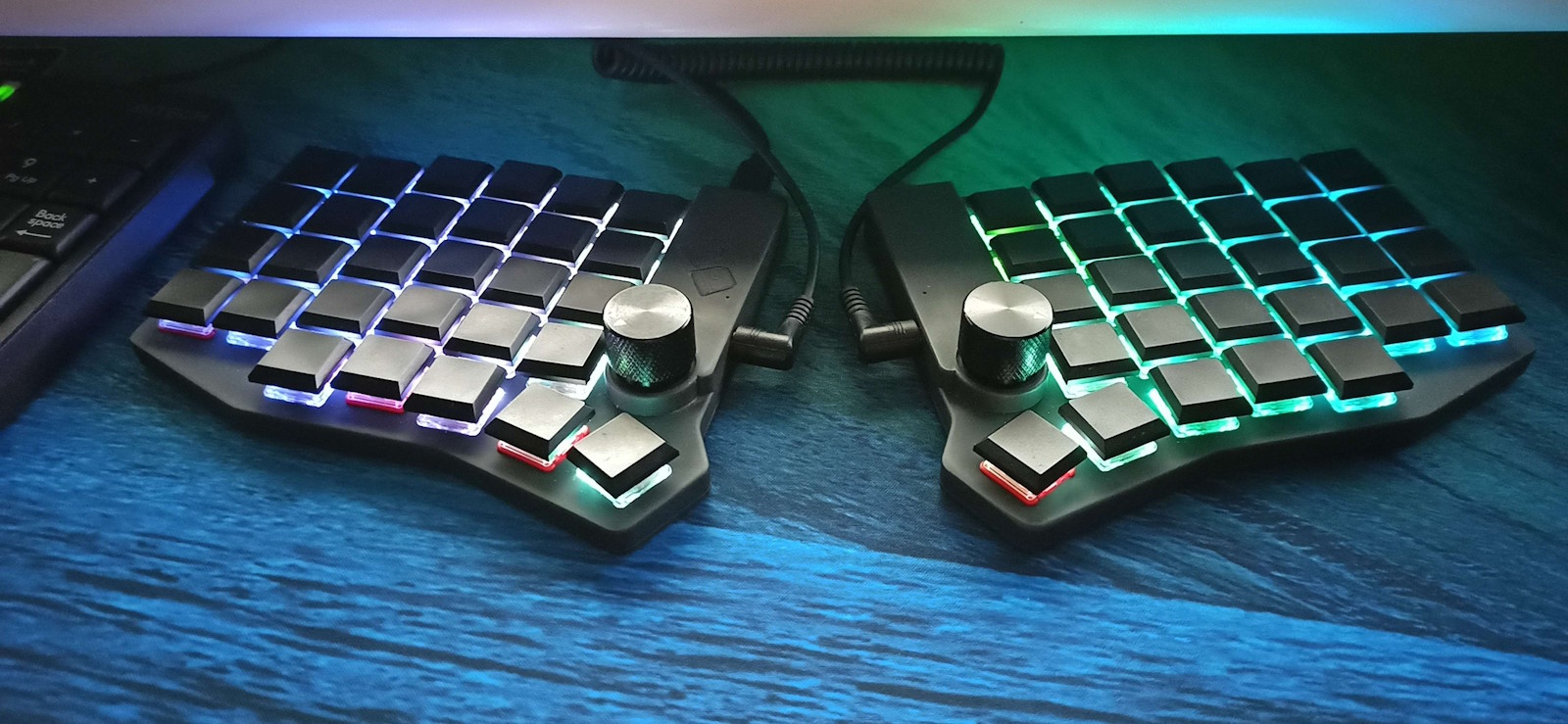 A Sofle Choc keyboard illuminates a matching desk mat in quiet green and blue tones. Some of the keys have different base colors.